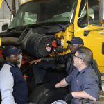 two diesel tech students working with instructor on yellow tractor