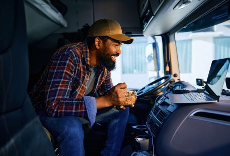 image of truck driver taking a break while eating lunch and using his computer in the truck cab