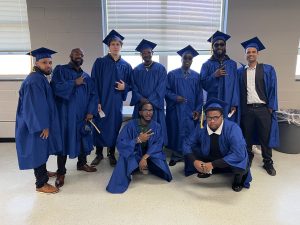 Nine graduates smiling and holding up peace signs