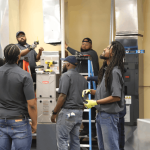 Group of HVAC students and instructors gathered around HVAC equipment