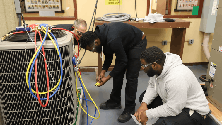 Three HVAC students crouched down and looking at electric wires for a HVAC system