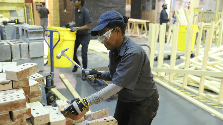 Construction student hammering a pile of bricks