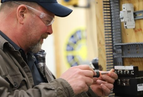 Trade school student wearing safety glasses working on an electrical component during electrician training