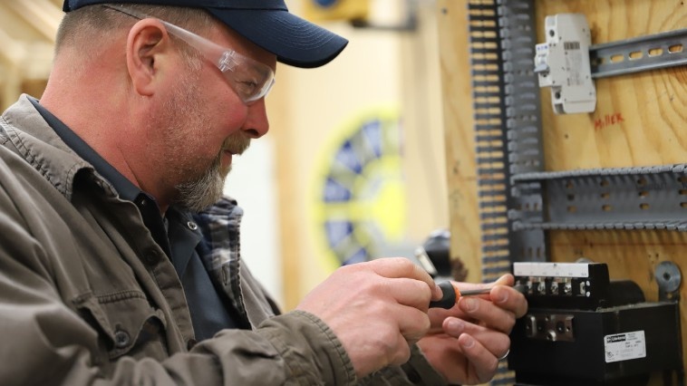 Trade school student wearing safety glasses working on an electrical component during electrician training