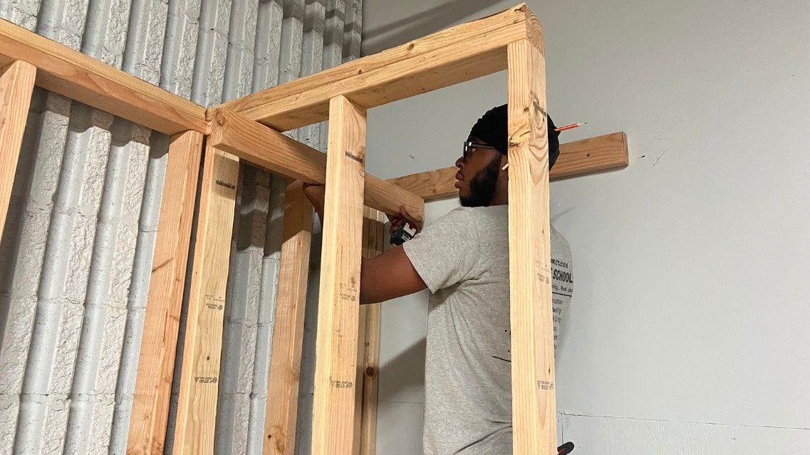 Building technology student using a nail gun on a wooden structure